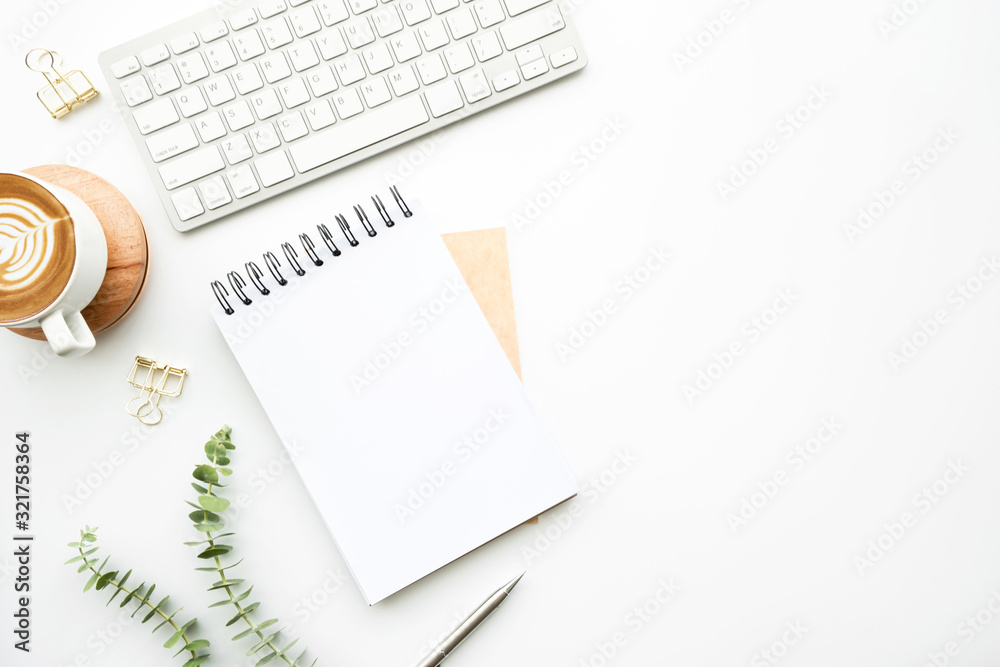 Blank notebook is on top of white minimal office desk table with cup of latte coffee and supplies. Top view with copy space, flat lay. - obrazy, fototapety, plakaty 