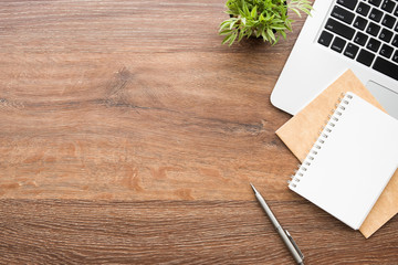 Wood office desk table with blank notebook with pen, laptop computer and supplies. Top view with copy space, flat lay.
