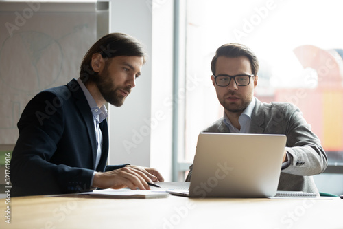 Two serious businessmen colleagues discussing project, looking at laptop screen