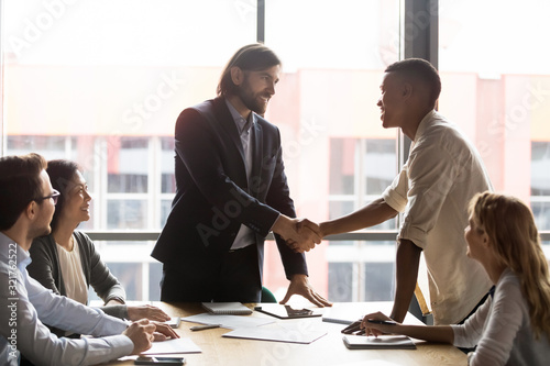 Confident smiling executive shaking African American employee hand at meeting