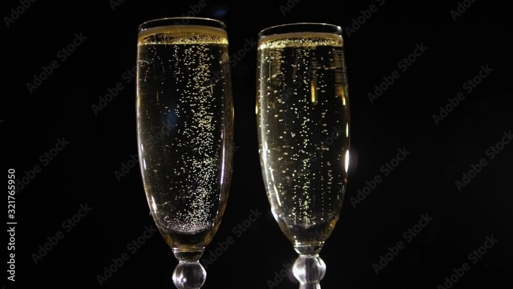 Two glasses of champagne with bubbles slowly rotating on a black