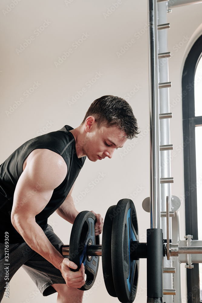 Bodybuilder putting steel plates on barbell before lifting weights in gym Bodybuilder putting steel plates on barbell before lifting weights in gym