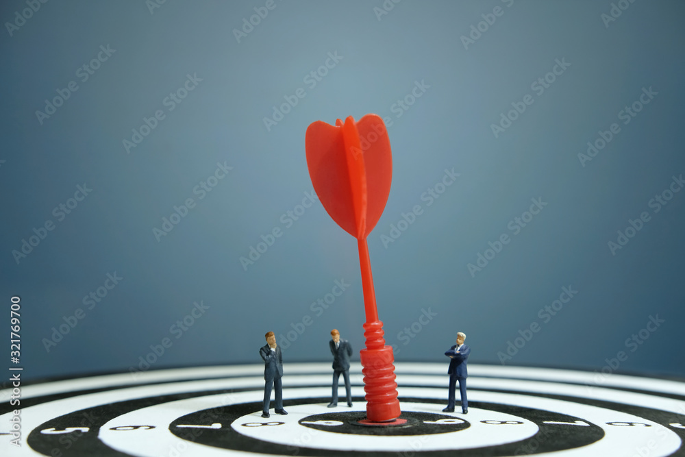Business strategy conceptual photo - Miniature of businessman discussion on dartboard with embedded red arrow Business strategy conceptual photo - Miniature of businessman discussion on dartboard with embedded red arrow