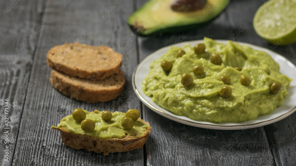 Whole-grain bread with guacamole and green peas on a black wooden table. Diet vegetarian Mexican food avocado. Whole-grain bread with guacamole and green peas on a black wooden table. Diet vegetarian Mexican food avocado.