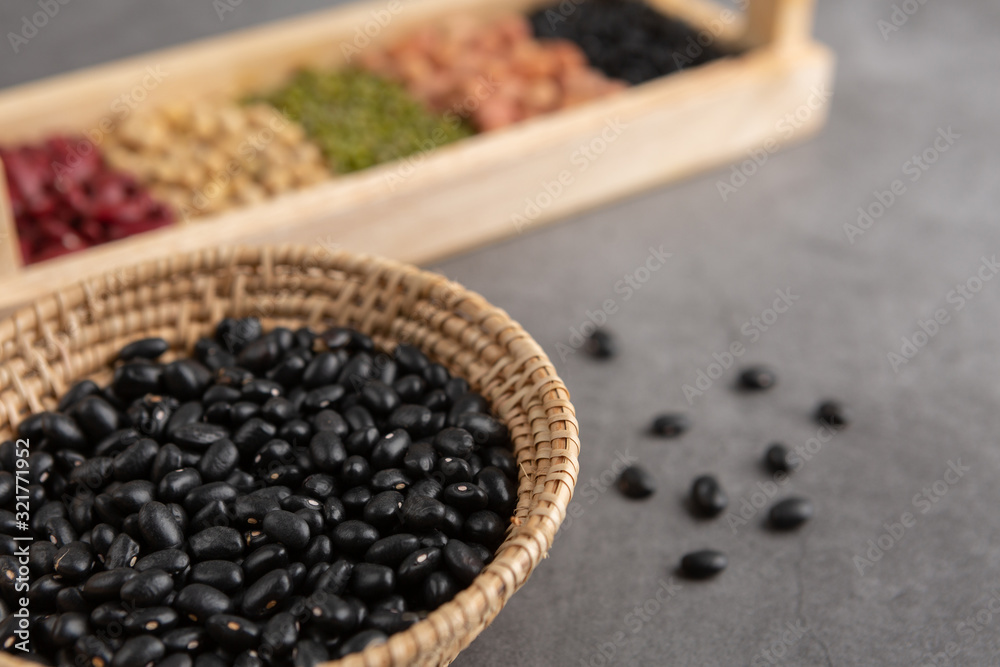 Black beans and grains in the wooden basket and in the wooden tray placed on the black cement floor. High angle view. Black beans and grains in the wooden basket and in the wooden tray placed on the black cement floor. High angle view.