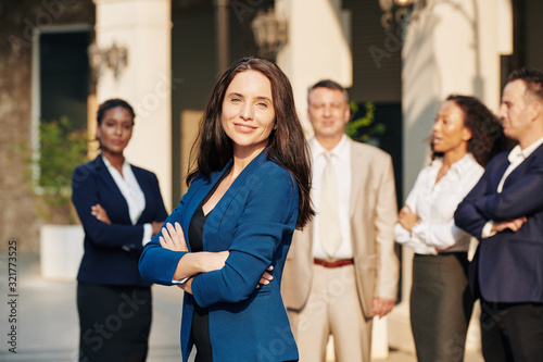 Beautiful successful female entrepreneur standing in front her business team and smiling at camera