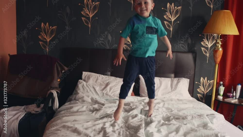 The boy makes high jumps on the double bed of his parents as if on a trampoline The boy makes high jumps on the double bed of his parents as if on a trampoline