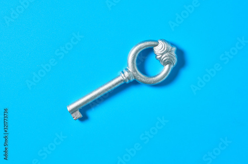 Single old antique silver key lies on blue color desk. Top view. Close-up © OlekStock