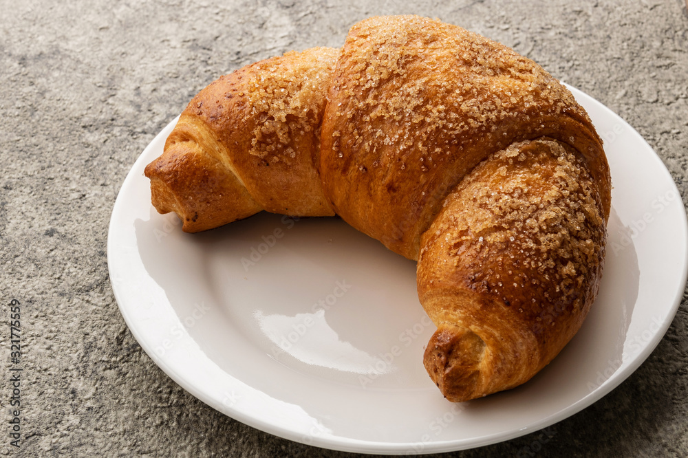 Croissant lies on a white plate. The plate is on a gray background. Croissant lies on a white plate. The plate is on a gray background.