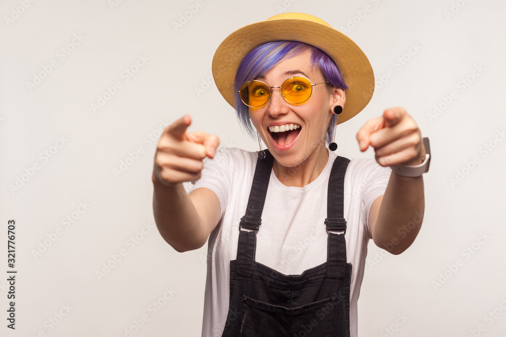 Hey, you are awesome! Portrait of amazed joyful glamour girl with violet hair in sunglasses and hat pointing to camera with two hands, choosing you. isolated on white background, indoor studio shot