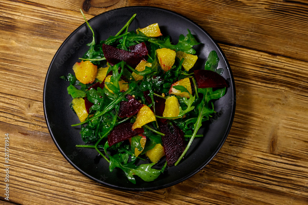 Tasty salad of fresh arugula, beetroot and oranges on wooden table. Top view. Healthy food or vegetarian concept Tasty salad of fresh arugula, beetroot and oranges on wooden table. Top view. Healthy food or vegetarian concept