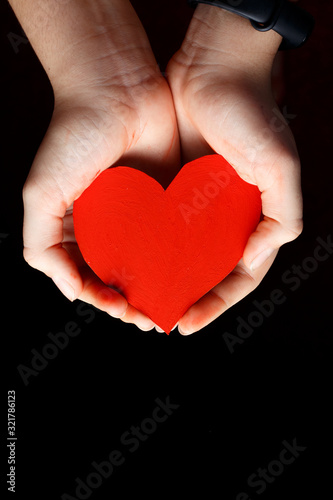 Red heart in the palms of a child against a dark background.