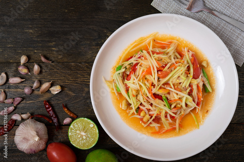 Papaya salad with chili and lemon in white dish on wooden table.(Som Tam Thai)
