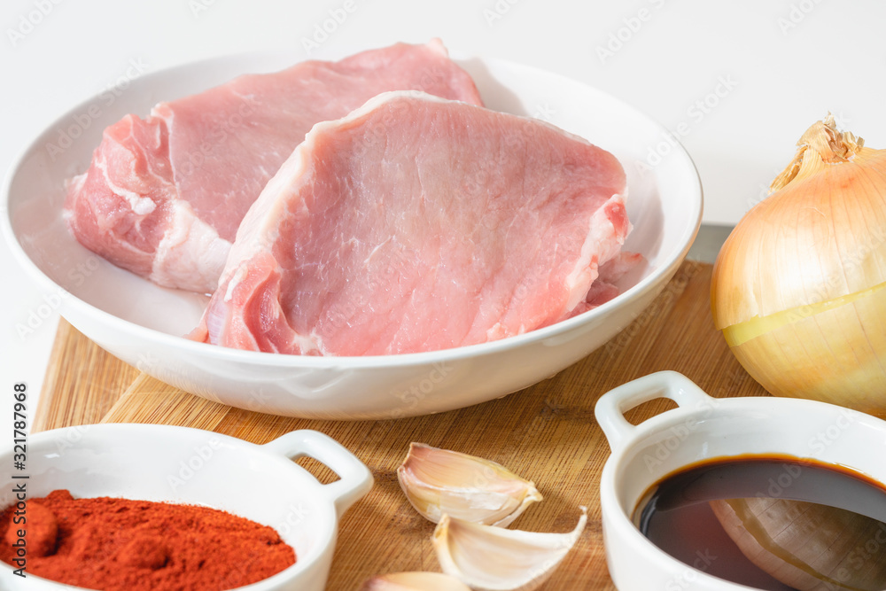 Fresh raw pork meat slices, garlic, onion, soy sauce, and some ingredients on a kitchen table, close up on white background Fresh raw pork meat slices, garlic, onion, soy sauce, and some ingredients on a kitchen table, close up on white background