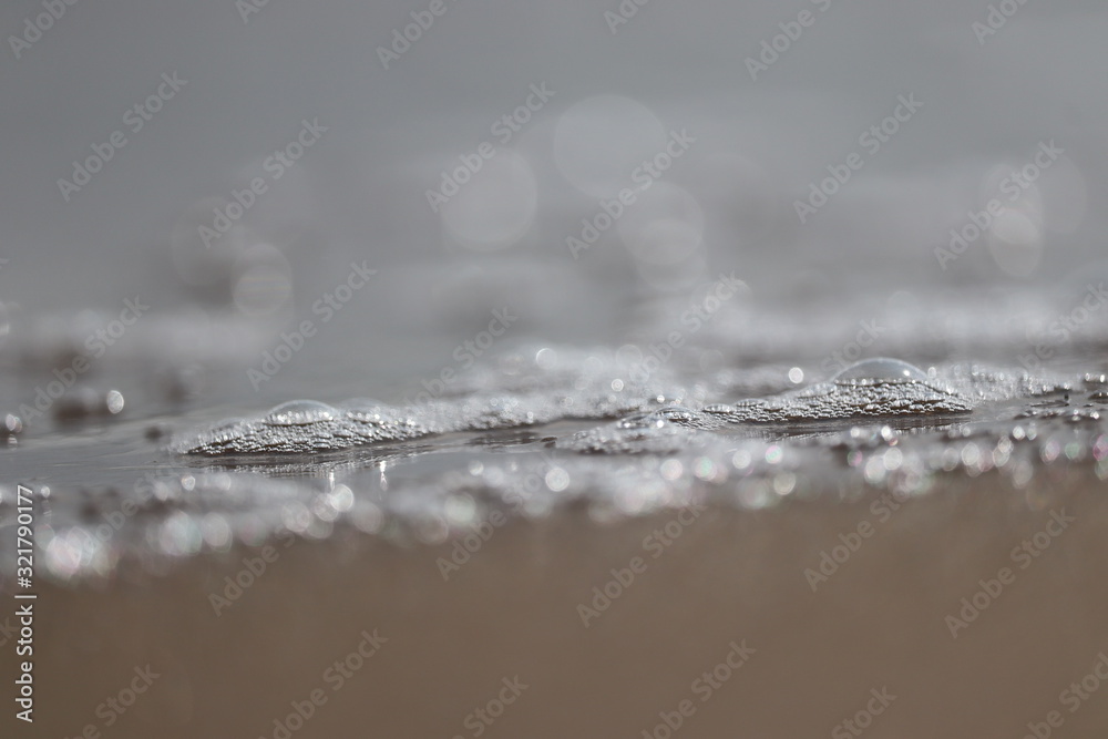 close up of white bubbles on water surface from beach with blur sandy background