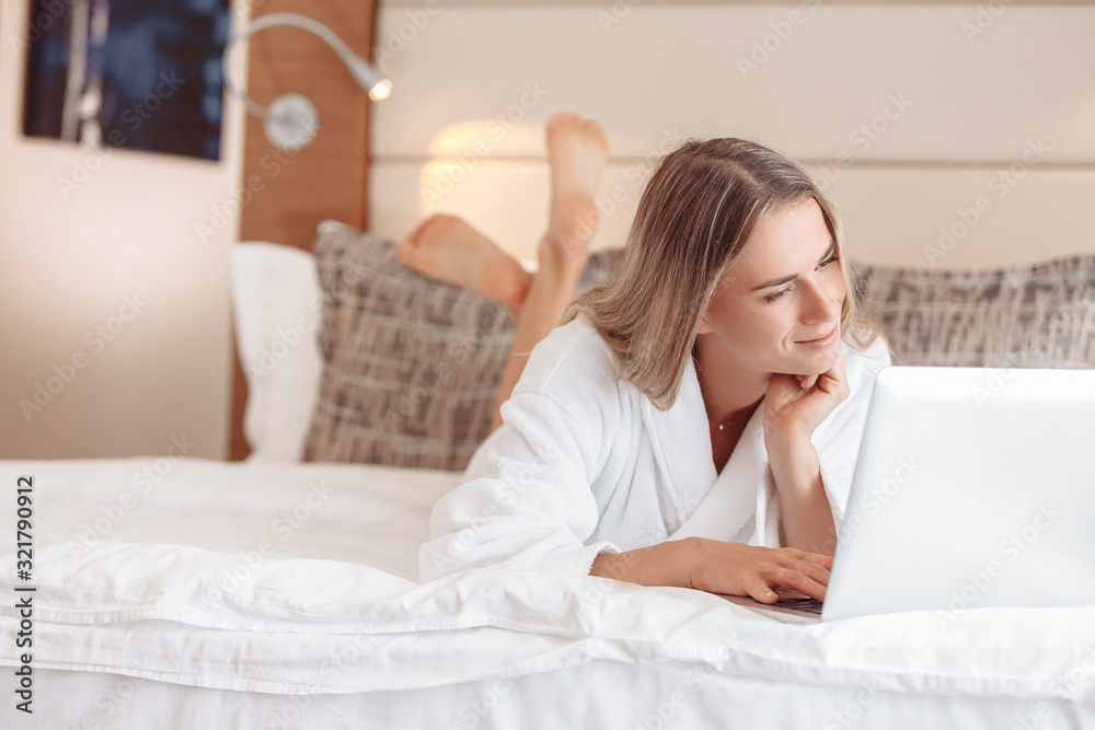 Cheerful beautiful young woman female student in white coat lies on bed and watch video lessons, training in Internet using laptop,high-speed internet. Concept of Additional education. Remote working Cheerful beautiful young woman female student in white coat lies on bed and watch video lessons, training in Internet using laptop,high-speed internet. Concept of Additional education. Remote working