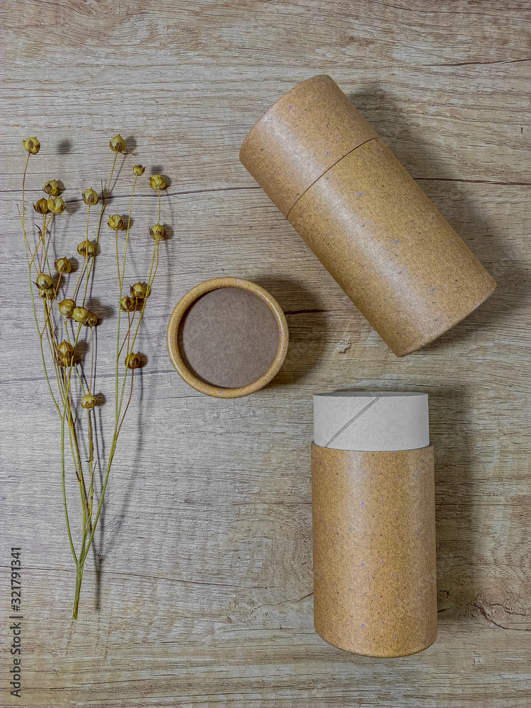 Paper or cardboard tube with paper cover on wooden background with dry flax. Flat lay recycle concept. Top view. Vertical mobile photo.