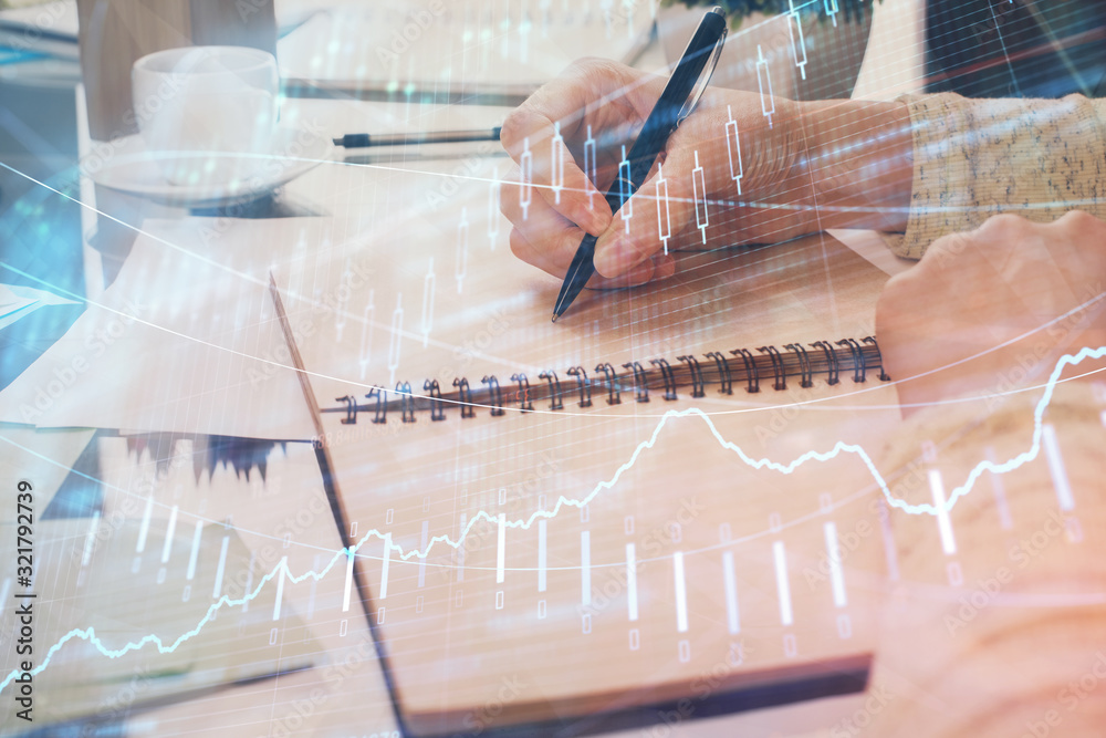Hand taking notes in notepad. Forex chart holograms in front. Concept of research. Double exposure