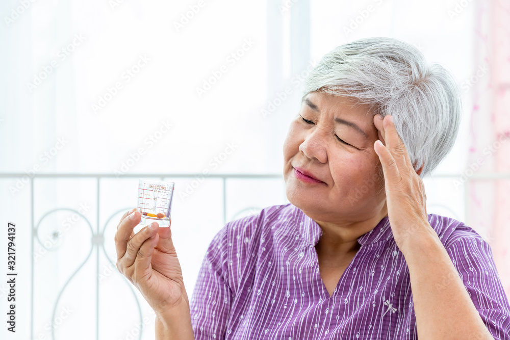 Senior elder woman female looking at measuring glass cup checking medicine, suffer from sickness Senior elder woman female looking at measuring glass cup checking medicine, suffer from sickness