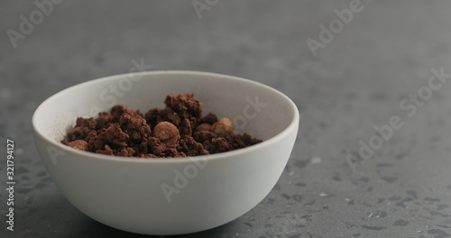 chocolate granola with nuts in white bowl on terrazzo surface