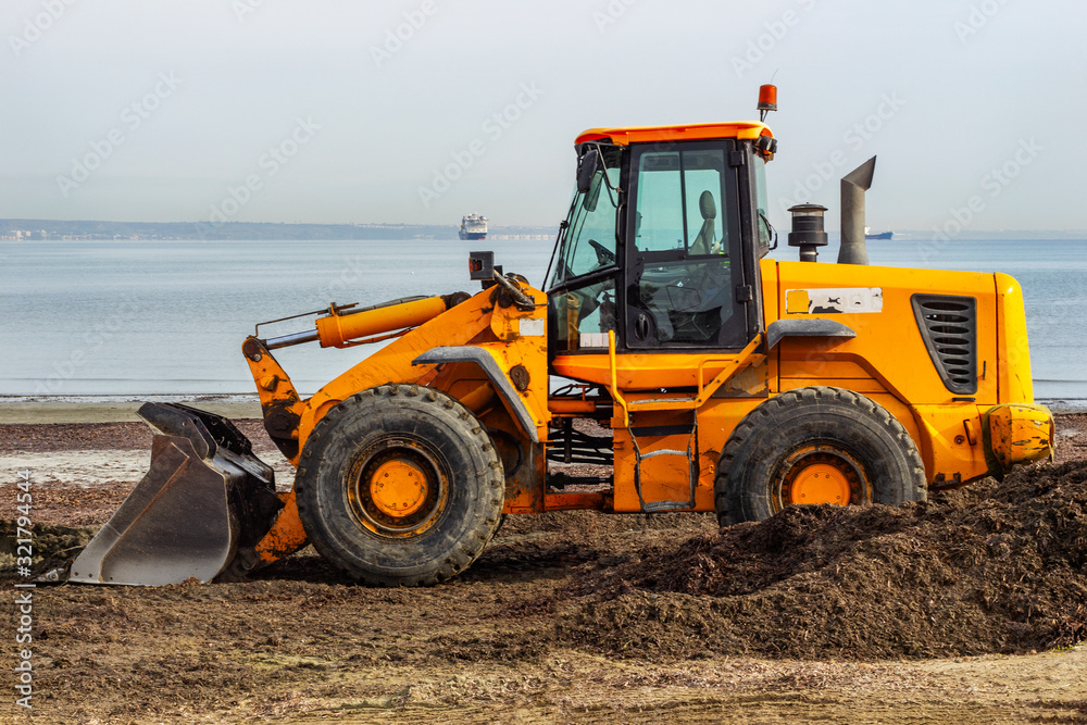 Yellow grader leveled the land by the sea. The process of preparing the beach for the summer season. Yellow grader leveled the land by the sea. The process of preparing the beach for the summer season.