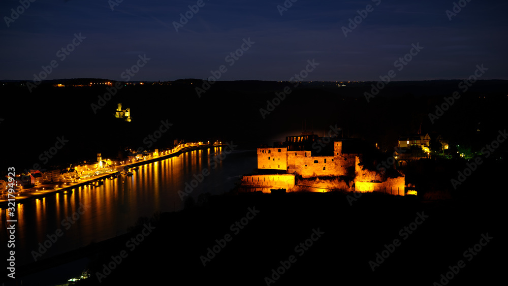 Night shot of Castle Rheinfels, colorfully illuminated, in front of the Rhine valley and under a starry sky. In background Castle Katz and the city of St.Goar