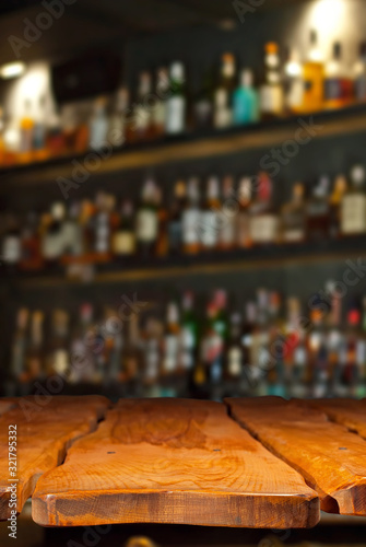 Wooden board on a background of bottles with alcohol. Old bar counter as layout for design. Workpiece for design. Empty place to advertise products. Blurred interior of the bar in the background.