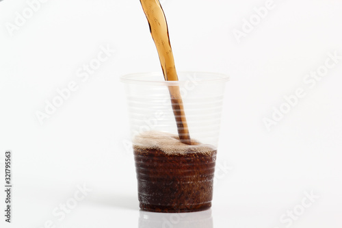 Pouring cola into plastic cup. Isolated on white background.