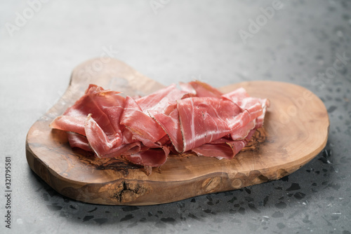 Sliced prosciutto ham on olive wood board