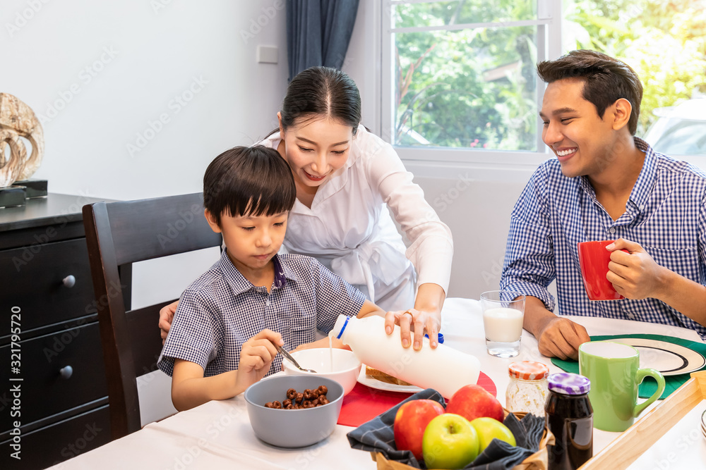 Happy Asian family in dining room, mother serving breakfast to father and son, mom pouring milk for boy