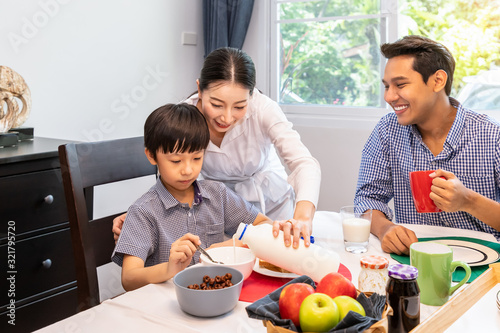Happy Asian family in dining room  mother serving breakfast to father and son  mom pouring milk for boy