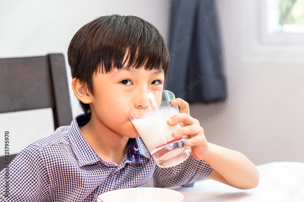 Adorable happy young Asian boy having breakfast and drinking milk at home in the morning; looking at camera Adorable happy young Asian boy having breakfast and drinking milk at home in the morning; looking at camera