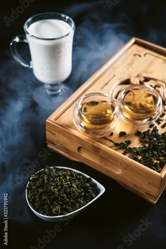 Chinese tea ceremony with glass cups with milk Oolong tea on wooden board and black background. Traditional Asian drink, beautiful serving