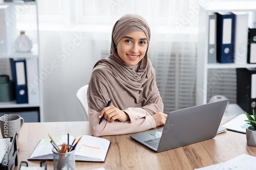 Millennial Muslim Girl In Headscarf Posing At Workplace In Modern Office