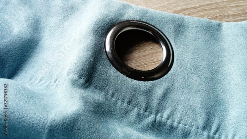 Metal grommet on a gray-blue velvet curtain. The fabric lies on a wooden table. The hole on the material is made of silver coated aluminum. Close-up of a metal eyelet photo