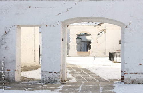 View of the porch of an old building through an arch in a white brick wall © MIKHAIL BATURITSKII	