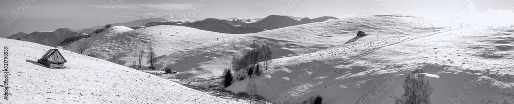 Obraz premium the rays of the sun over the mountains with snow and old derelict hut, Cindrel mountains, Paltinis, Romania. Monochromatic view.