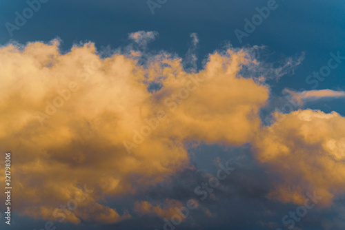 Stunning fluffy thunderstorm clouds illuminated by disappearing rays at sunset and dark cumulonimbus floating across sunny blue sky to change season weather. Natural abstract meteorology background.