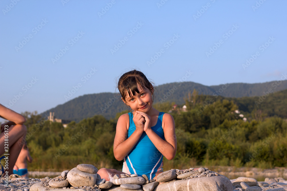 little girl in a swimsuit on the beach in the summer builds something pebble stones