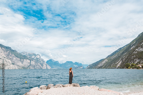 A woman in a long gray dress is standing on the rocky shore of Lake Garda. Italian landscape on a summer sunny day. photo
