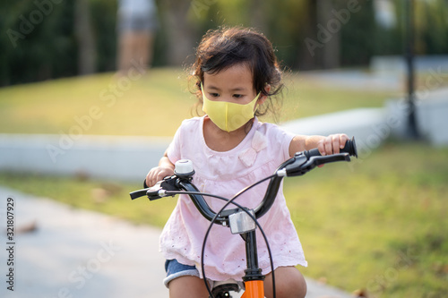 Little girl wearing anti pollution mask on her bike at park.