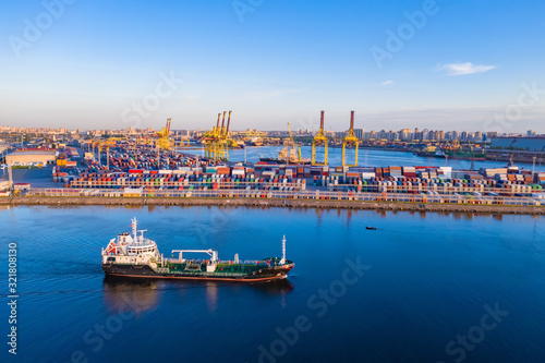 Cargo ship is on the fairway. Sea commercial port. On the pier are containers with goods. Cranes carry out loading and unloading. Transportation of goods by sea. Panorama of the port.
