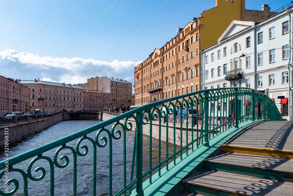 Bridge with green railings and steps in the center of St. Petersburg. Bridges Of St. Petersburg. The bridge connects the banks of the canal. Landscape of the cozy city on a Sunny day.