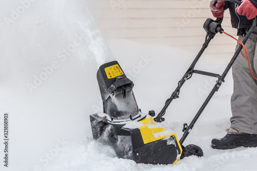 Man is brushing white snow with the yellow electric snow thrower in a winter garden © Tatiana Kuklina