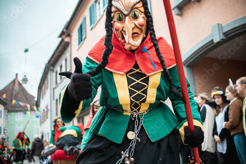 Freiburger Hexen - Hexe mit Katzenaugen im grün, gelb, rotem Gewand zeigt Daumen hoch. Bei Fastnachtsumzug in Staufen Süd Deutschland.