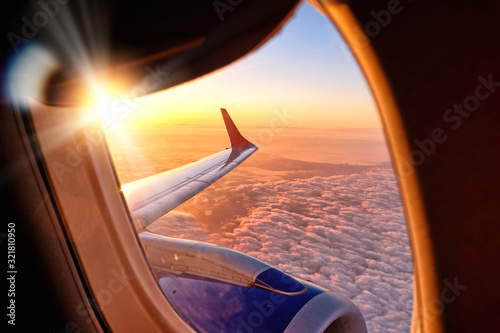 plane wing from airplane window seat in flight nature landscape against scenic sunset sky background. Aerial view from aircraft passenger cabin on beautiful red orange sunrise cloudscape and blue sky