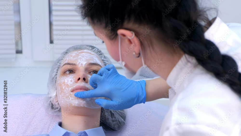 Cosmetologist is applying cream with anesthesia on patient's face skin before biorevitalization procedure. Woman in beauty clinic with doctor beautician preparing to treatment using numbing cream. Cosmetologist is applying cream with anesthesia on patient's face skin before biorevitalization procedure. Woman in beauty clinic with doctor beautician preparing to treatment using numbing cream.