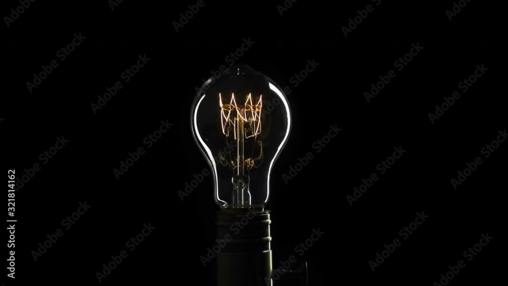 Real Edison light bulb flickering. Vintage filament Edison light bulb. Close up. 4K UHD video. Symbol of idea. The light comes on on a black background.