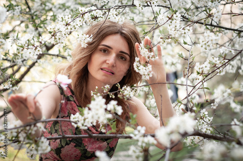 soft focus of beautiful confident woman between branches with white blooming flowers looking at camera in garden