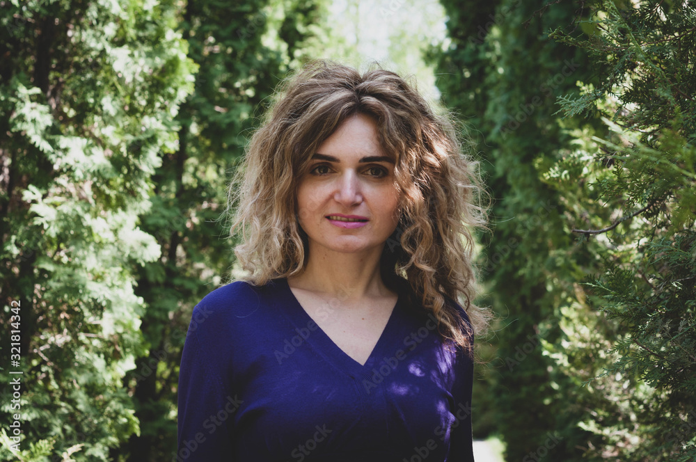 soft focus of portrait of beautiful cheerful woman with long hair in front of green thuja looking at camera in garden soft focus of portrait of beautiful cheerful woman with long hair in front of green thuja looking at camera in garden